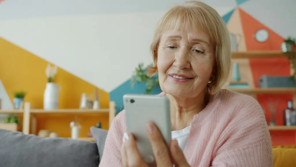 Mujer mayor sonriendo mientras usa su celular en el sofá de su casa
